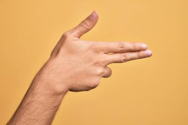 İzole edilmiş sarı arka planda parmaklarını gösteren beyaz bir gencin eli. Ateşli silahı parmaklarıyla işaret ediyor.
