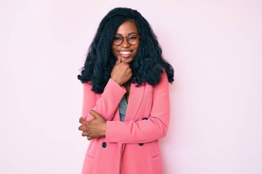 İş ceketi ve gözlük takan güzel Afrikalı kadın kameraya kendinden emin bakıyor kollarını kavuşturmuş ve çenesini kaldırmış gülümsüyor. Olumlu düşünmek. 