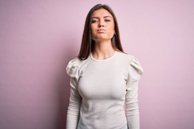 Mavi gözlü genç ve güzel bir kadın pembe arka plan üzerine günlük beyaz tişört giyip komik yüzlü yanakları şişiriyor. Havayla şişmiş ağız, çılgın bir ifade..