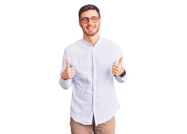 Zarif iş gömleği ve gözlük takan yakışıklı genç adam. Elleriyle olumlu jest yapıyor. Gülümsüyor ve mutlu. Neşeli ifade ve kazanan jest. 