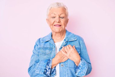 Mavi gözlü, gri saçlı, sıradan bir kot ceket giyen, göğsünde elleri kapalı, yüzünde minnet ifadesi olan son sınıf güzeli bir kadın. sağlık kavramı. 