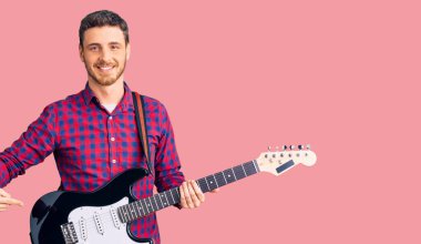 Elektro gitar çalan yakışıklı genç adam mutlu bir şekilde elini ve parmağını gösterdi. 