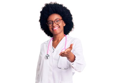 Young african american woman wearing doctor coat and stethoscope smiling cheerful offering palm hand giving assistance and acceptance.  clipart