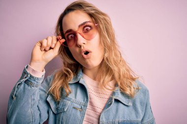 Kot ceket ve kalp şeklinde güneş gözlüğü takan güzel bir kadın. Şoktan korkmuş, korkmuş ve korku ifadesinden heyecanlanmış.