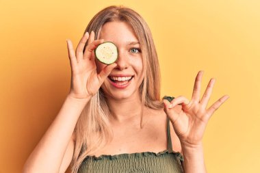 Sarışın, güzel bir kadın, salatalık sümüğünü tutuyor. Parmaklarıyla işaret veriyor, gülümsüyor. Mükemmel bir sembol. 