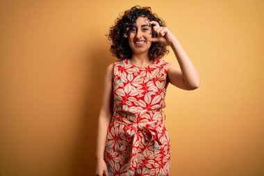 Genç, güzel, kıvırcık Arap kadın tatilde. Çiçekli bir elbise giyiyor, güneş gözlüğü takıyor, gülümsüyor ve el hareketleriyle küçük boy işaretler yapıyor. Ölçü kavramı.