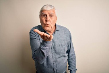 Senior handsome hoary man wearing casual shirt standing over isolated white background looking at the camera blowing a kiss with hand on air being lovely and sexy. Love expression. clipart