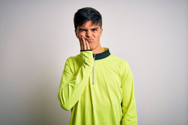 Spor yapan yakışıklı genç sporcu, diş ağrısı ya da diş ağrısı yüzünden izole edilmiş beyaz arka plan üzerine spor giyerek ağız ve acı dolu yüz ifadelerine dokunuyor. Dişçi