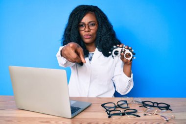 Elinde optometri gözlüğü olan güzel Afrikalı bir kadın kamerayı ve seni işaret ediyor. Kendine güvenen bir jest, ciddi görünüyor. 
