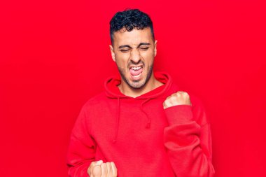 Gündelik giysiler giyen genç İspanyol adam şaşkınlık ve şaşkınlık içinde kollarını kaldırarak ve gözlerini kapayarak başarıyı kutluyor. 