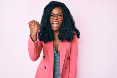 Güzel Afrikalı bir kadın iş ceketi ve gözlük takıyor kızgın ve kızgın. Öfkeyle bağırırken yumruğunu kaldırıyor. öfke ve agresif konsept. 