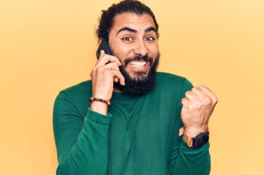 Genç Arap adam telefonda konuşuyor gururla bağırıyor, zaferi kutluyor ve kollarını kaldırarak heyecanlanıyor. 