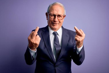 Grey haired senior business man wearing glasses and elegant suit and tie over purple background Showing middle finger doing fuck you bad expression, provocation and rude attitude. Screaming excited