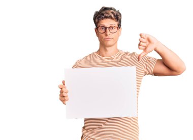 Genç yakışıklı adam boş pankart tutuyor kızgın yüzlü, negatif işaret baş parmakları aşağıda, reddedilme konsepti 