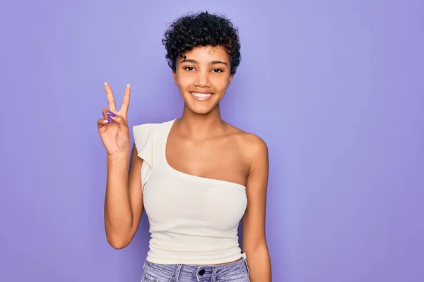年轻美丽的非洲裔美国女人穿着休闲T恤 背景是紫色的 微笑着看着摄像机 手指在做胜利的标志 第二点 — 图库照片