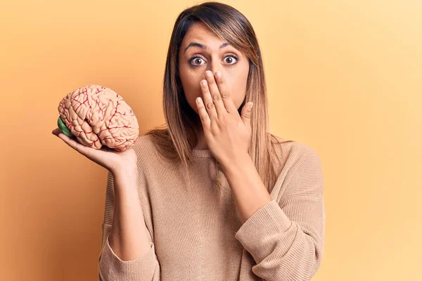 Young beautiful woman holding brain covering mouth with hand, shocked and afraid for mistake. surprised expression