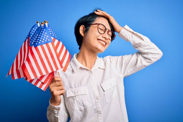Young beautiful asian patriotic girl holding united states flags celebrating independence day stressed with hand on head, shocked with shame and surprise face, angry and frustrated. Fear and upset for mistake.