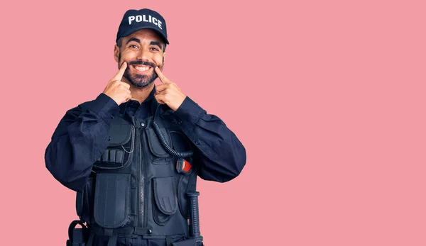 Young hispanic man wearing police uniform smiling with open mouth, fingers pointing and forcing cheerful smile