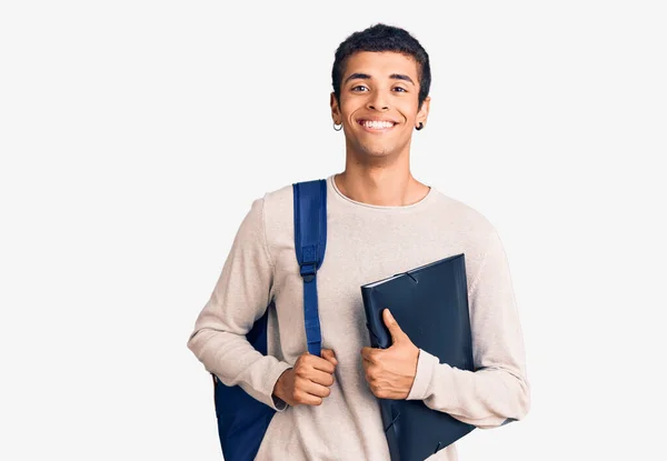 若いアフリカ系アメリカ人の男を着て学生のバックパックを保持バインダー見て正と幸せな立ちと笑顔で自信を持って笑顔を示す歯 — ストック写真