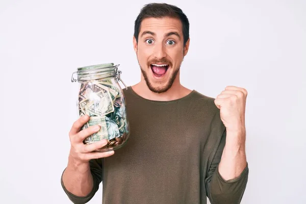 Joven Hombre Guapo Sosteniendo Frasco Con Ahorros Gritando Orgulloso Celebrando —  Fotos de Stock