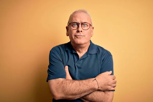 Middle age handsome hoary man wearing casual polo and glasses over yellow background shaking and freezing for winter cold with sad and shock expression on face