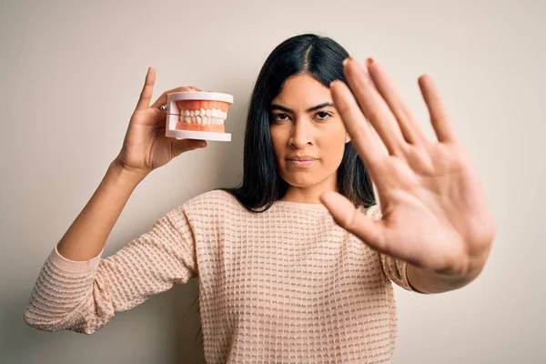 stock image Young beautiful hispanic dentist woman holding prosthesis dental mouth with open hand doing stop sign with serious and confident expression, defense gesture