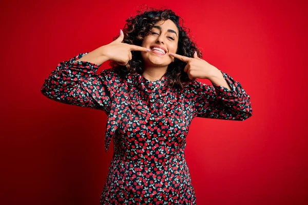 年轻美丽的卷曲阿拉伯女人 身穿休闲装 站在红色的背景上 笑容满面 用手指 牙齿和嘴指尖 牙齿健康概念 — 图库照片