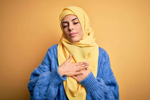 年轻美丽的黑发穆斯林女子 头戴阿拉伯头巾 头戴黄褐色头巾 双手放在胸前 闭着眼睛 脸上挂着感激的手势 健康概念 — 图库照片