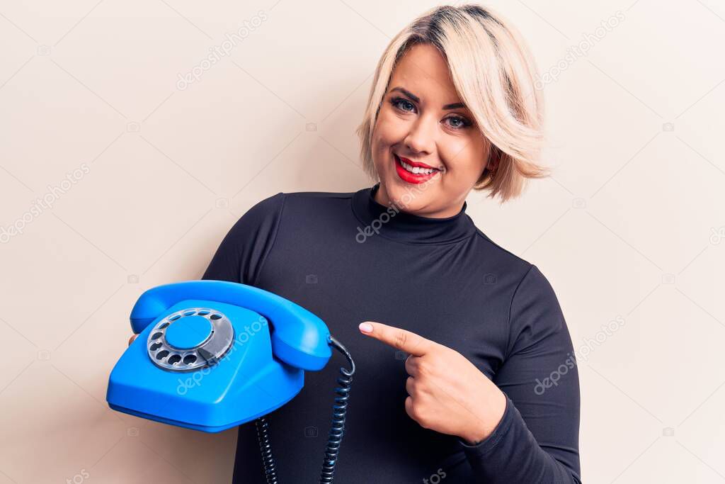 Young beautiful plus size woman holding vintage telephone over isolated white background smiling happy pointing with hand and finger
