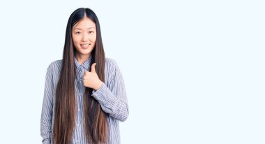 Genç, güzel, Çinli bir kadın, gündelik tişörtler giyip, el hareketleriyle mutlu mesut bir jest yapıyor. Kameraya bakıp başarıyı gösteren ifade. 