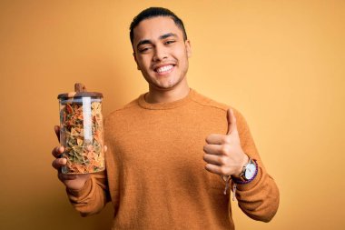 Elinde İtalyan makarnası olan genç Brezilyalı bir adam izole edilmiş sarı arka planda mutlu bir şekilde gülümsüyor.