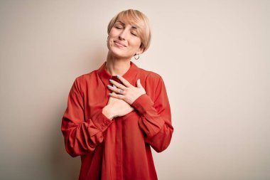 Genç ve güzel iş kadını sarışın bir kadın izole edilmiş arka planda ayakta duruyor elleri göğsünde, gözleri kapalı ve yüzünde minnet dolu bir jest ile. Sağlık kavramı.