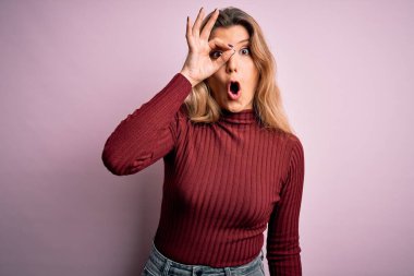 Genç, güzel, sarışın bir kadın pembe arka planda rahat bir süveter giyiyor. Şaşırmış yüz ifadesiyle, parmaklarından bakan gözleriyle şaşırmış bir hareket yapıyor. İnançsız ifade.