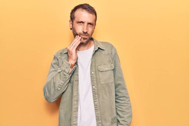 Sıradan kıyafetler giyen genç yakışıklı bir adam diş ağrısı ya da diş hastalığından dolayı acı dolu bir ifadeyle ağıza dokunuyor. dişçi 