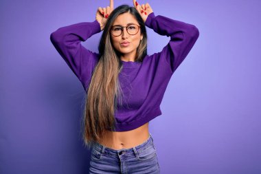 Genç, güzel, zeki bir kadın, mor gözlüklü, izole edilmiş arka planda komik hareketler yapıyor.