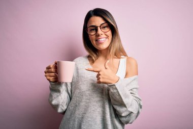 Genç, güzel, esmer, gözlüklü, pembe kahve fincanı içen, mutlu, eli ve parmağı olan bir kadın.