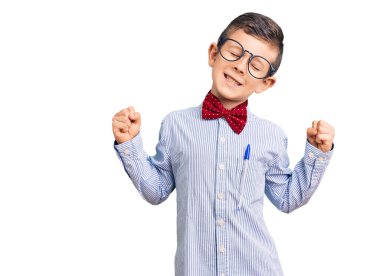 Sevimli sarışın çocuk inek papyonu takıyor ve gözlük takıyor. Çok mutlu ve heyecanlı. Kolları havada, gülümseyen ve başarı için çığlık atan kazanan bir jest yapıyor. kutlama konsepti. 