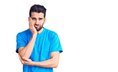 Sakallı, sıradan tişörtlü, yorgun görünen ve depresyondan sıkılmış kolları çaprazlanmış genç yakışıklı bir adam.. 