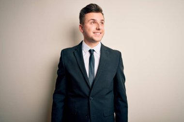 Zarif takım elbiseli ve kravatlı genç yakışıklı iş adamı yalıtılmış arka planda, yüzünde gülümseme, doğal bir ifade ile yan yana bakıyor. Kendinden emin gülen.