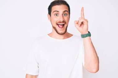 Gündelik beyaz t-shirt giyen genç yakışıklı adam başarılı bir fikri işaret ediyor. Heyecanlı ve mutlu. Bir numara.. 