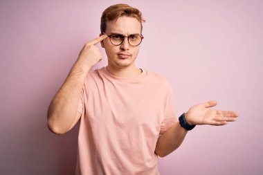 İzole edilmiş pembe arka plan üzerinde duran sıradan tişörtlü genç ve yakışıklı bir adam. Avuç içini açıp fotokopi alanını göstermekten ve alnını işaret etmekten rahatsız oluyor. Bunu bir düşün..