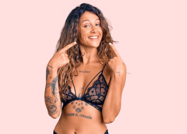 İç çamaşırı giyen, gülümseyen, parmaklarıyla ve ağzıyla işaret eden Latin kökenli genç bir kadın. diş sağlığı kavramı. 