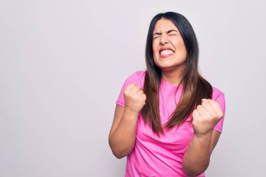 Genç, güzel, esmer, sıradan pembe tişörtlü bir kadın beyaz arka planda dikilmiş, kolları havada ve gözleri kapalı bir şekilde başarıyı kutluyor. Kazanan konsept.