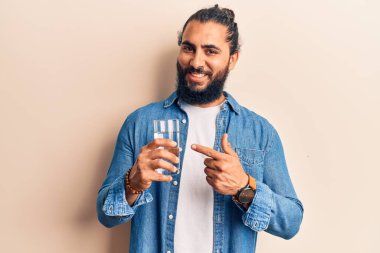 Genç Arap adam bir bardak su içerken mutlu bir şekilde el ve parmağınla işaret ediyor. 