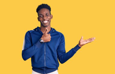 Afro-Amerikalı genç bir adam spor giyer, avuç içini gösterir ve baş parmaklarıyla iyi bir jest yapar, mutlu ve neşeli gülümser. 