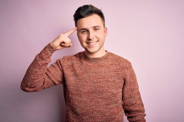 Pembe izole edilmiş arka plan üzerine sıradan bir kazak giyen yakışıklı beyaz bir adam tek parmağıyla gülümseyerek, harika bir fikir ya da düşünceyle, iyi bir hafızayla.