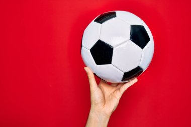 Güzel bir el futbol topunu izole edilmiş kırmızı arka planda tutuyor.