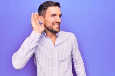 İzole edilmiş mor arka planda dikilen sıradan çizgili tişört giyen genç ve yakışıklı bir adam kulağının dibinde dedikodu ve dedikoduları dinliyor ve dinliyordu. Sağırlık kavramı.