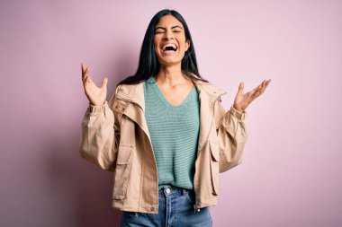 Kışlık ceket ve pembe arka plan üzerine kazak giyen genç, güzel İspanyol moda kadını kollarını kaldırmış ve gözleri kapalı heyecanla haykırarak başarıyı kutluyor. Kazanan konsept