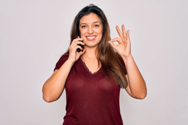 Genç İspanyol kadın, izole bir arka planda akıllı telefondan konuşuyor. Parmaklarıyla imza atıyor. Mükemmel bir sembol.